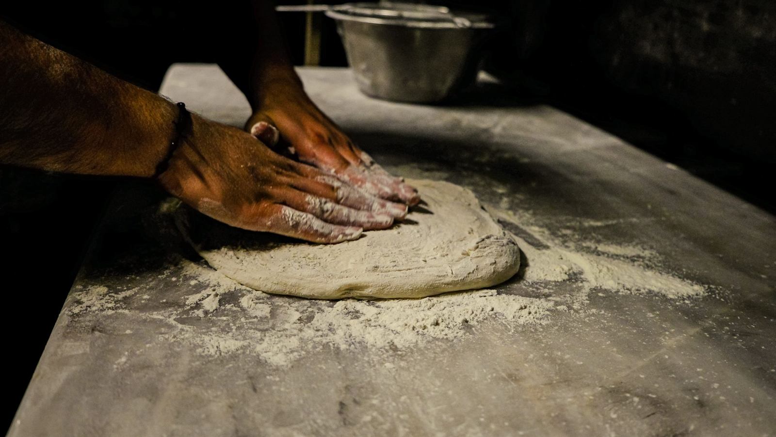 Mains de pizzaiolo pétrissant la pâte sur un plan fariné