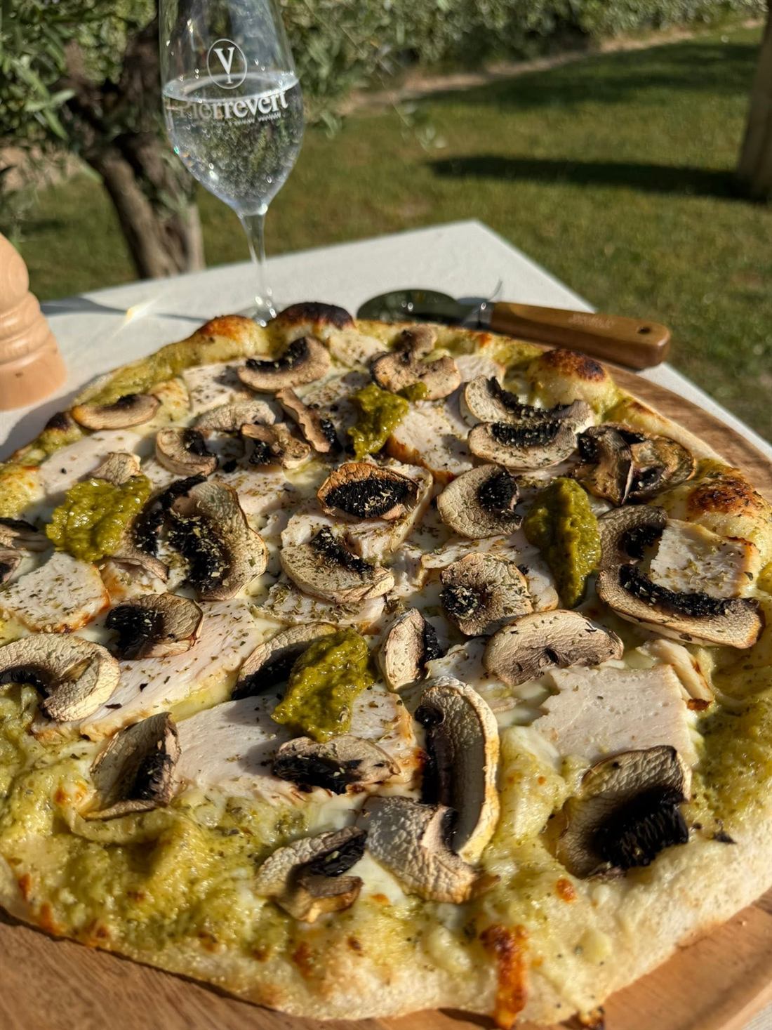 Pizza poulet pesto aux champignons, posée sur une planche en bois